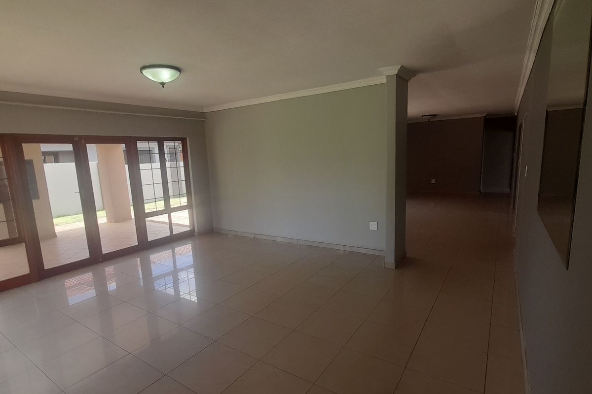 Spacious, empty living area featuring neutral tiled flooring, modern grey walls, and large sliding glass doors providing access to the outdoor patio.