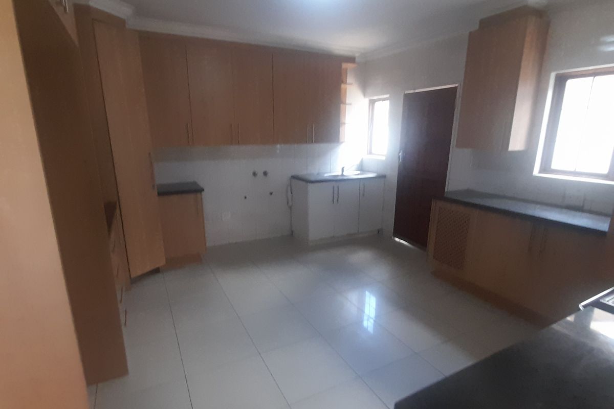 A spacious, empty kitchen featuring light wood-toned built-in cabinetry, dark countertops, and tiled flooring, offering a functional layout ready for customization.