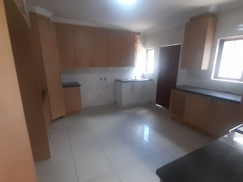 A spacious, empty kitchen featuring light wood-toned built-in cabinetry, dark countertops, and tiled flooring, offering a functional layout ready for customization.