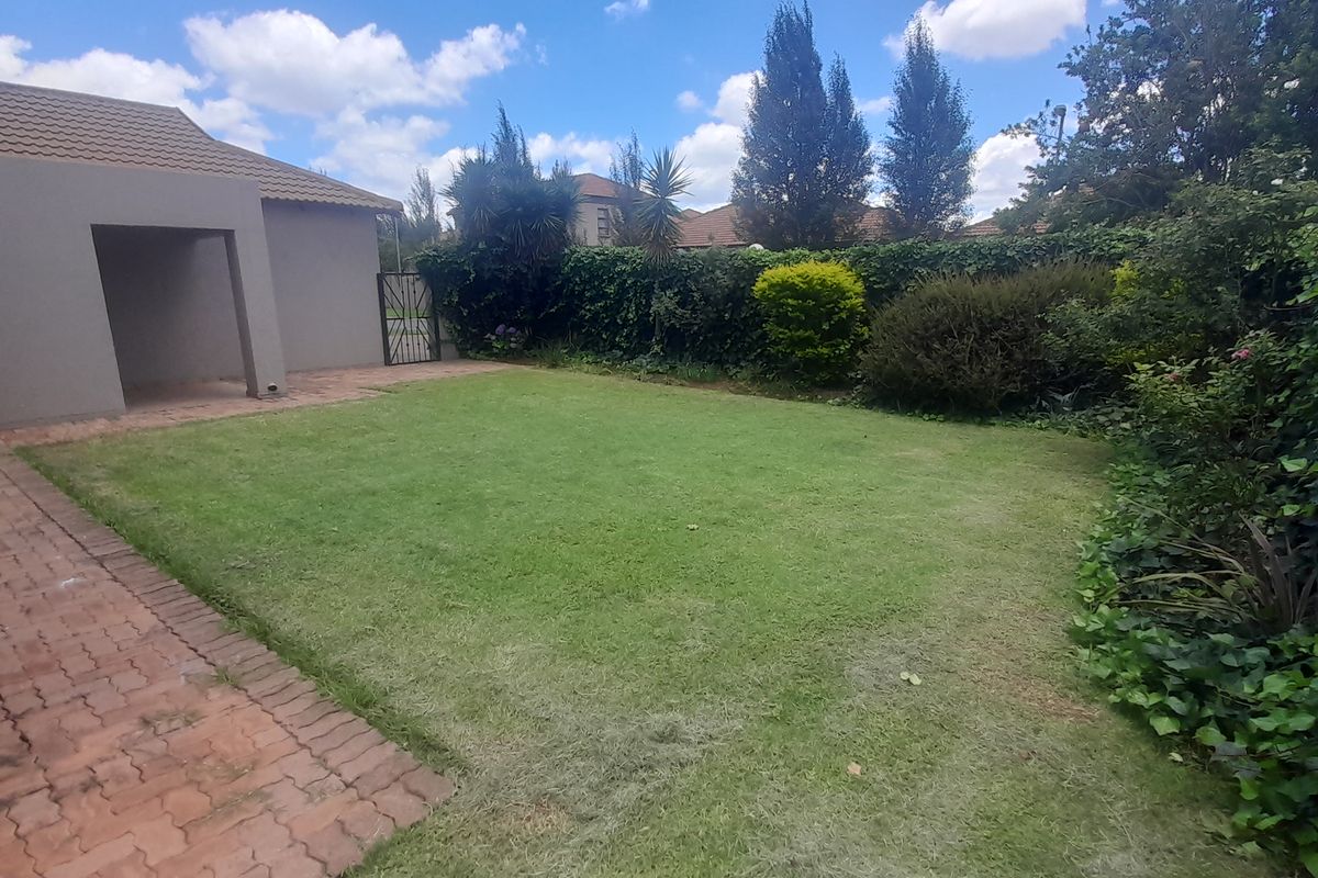A well-maintained rear garden featuring a paved patio area, a neat lawn, and established perimeter hedging.