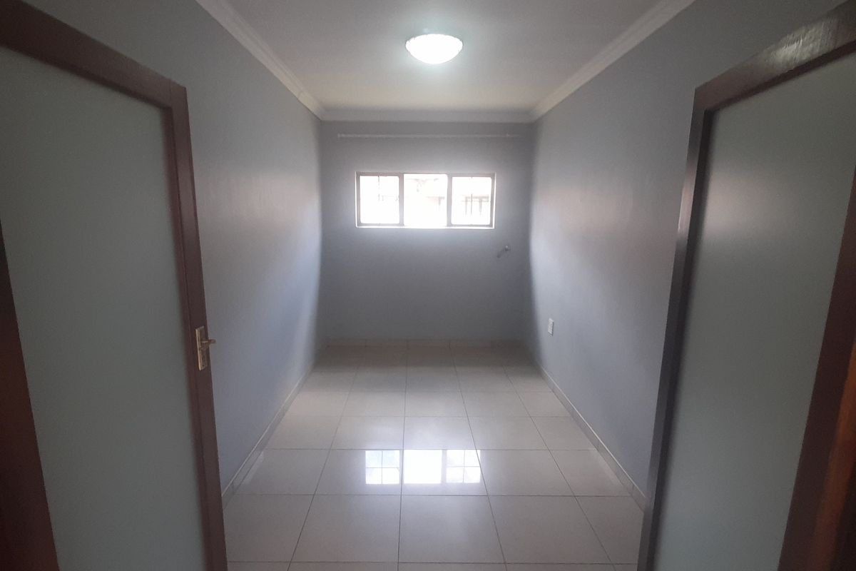 An empty, well-maintained bedroom featuring neutral grey walls, tiled flooring, and a central ceiling light fixture.