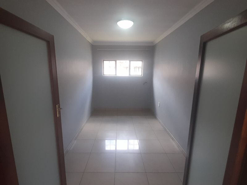 An empty, well-maintained bedroom featuring neutral grey walls, tiled flooring, and a central ceiling light fixture.