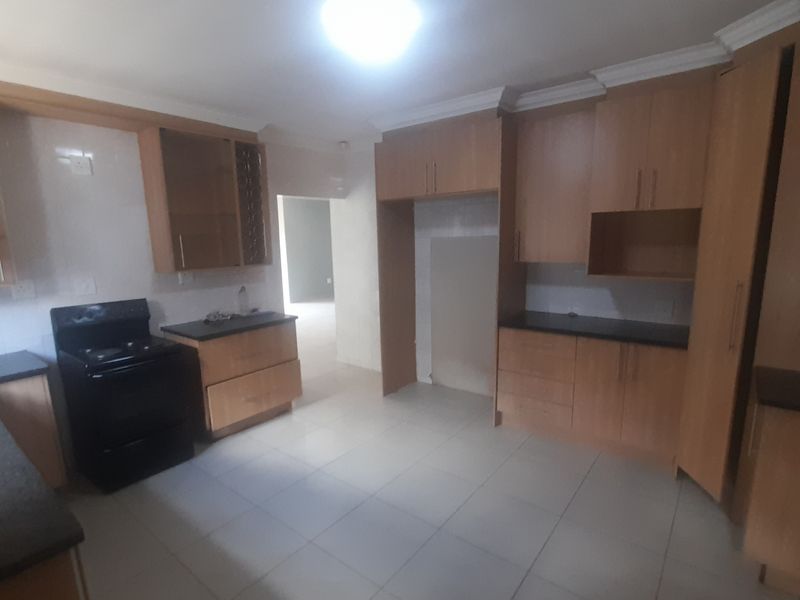 A spacious kitchen featuring wooden cabinetry, black countertops, and tiled flooring, offering a functional layout with space for a fridge and stove.