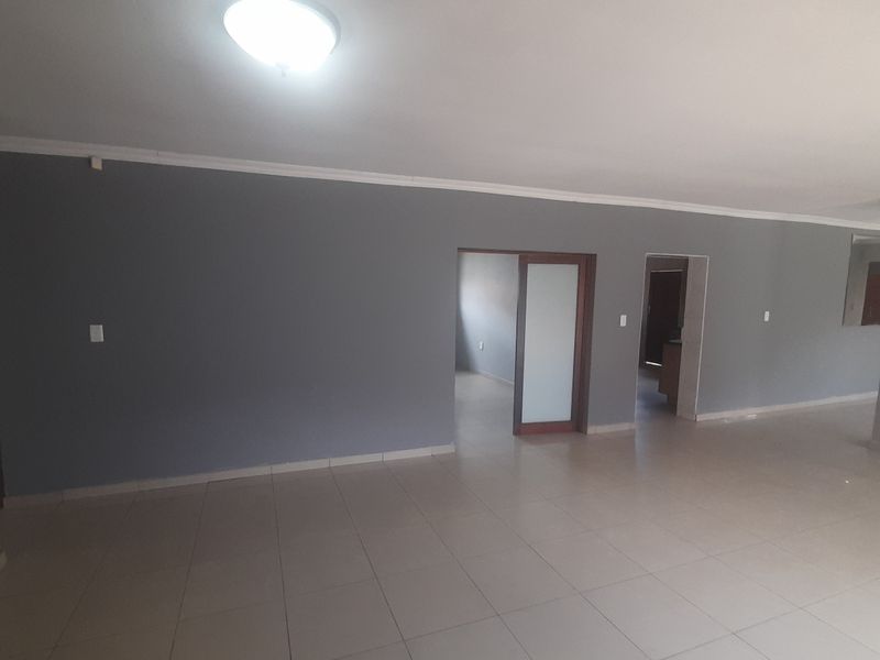 A spacious, empty living area featuring neutral grey walls, tiled flooring, and a sliding door leading to adjacent rooms.