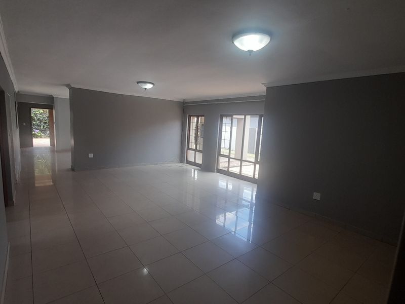 A spacious, empty living area featuring neutral grey walls, polished tiled flooring, and large sliding glass doors providing natural light and garden access.