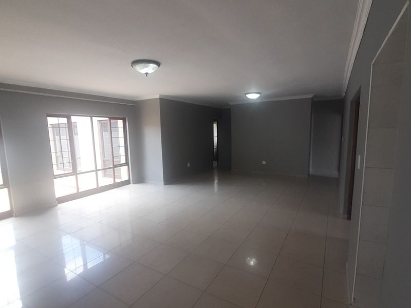A spacious, empty living area featuring neutral grey walls, polished tiled flooring, and large glass sliding doors providing ample natural light.