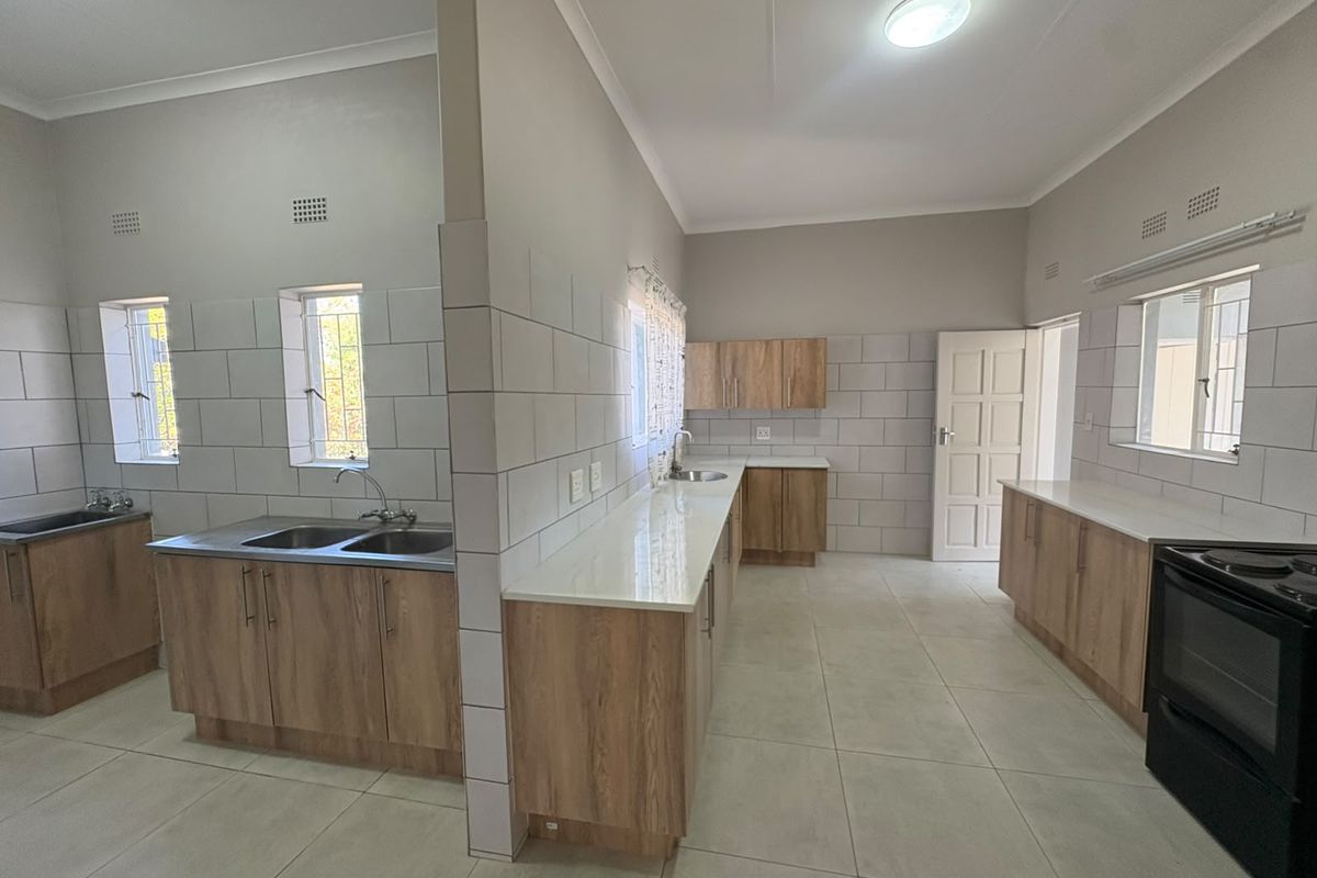 Spacious, modern kitchen featuring extensive built-in cabinetry, stone countertops, double sink, and tiled finishes throughout. The area is clean and ready for use.