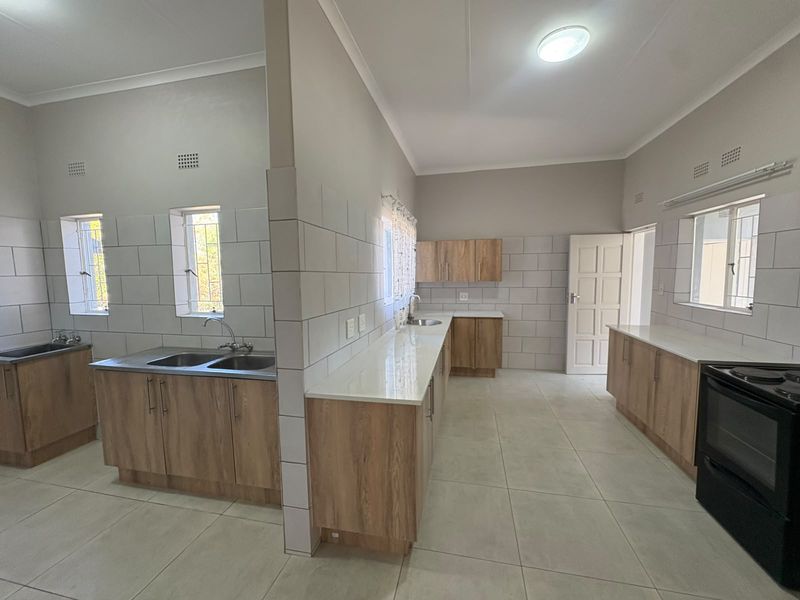 Spacious, modern kitchen featuring extensive built-in cabinetry, stone countertops, double sink, and tiled finishes throughout. The area is clean and ready for use.