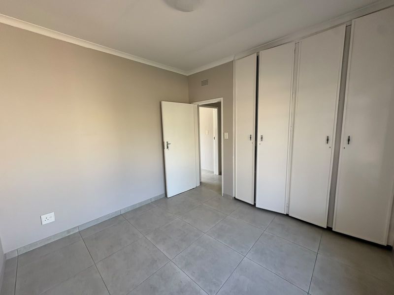 A clean, empty bedroom featuring neutral wall tones, large-format floor tiles, and ample built-in cupboard storage.
