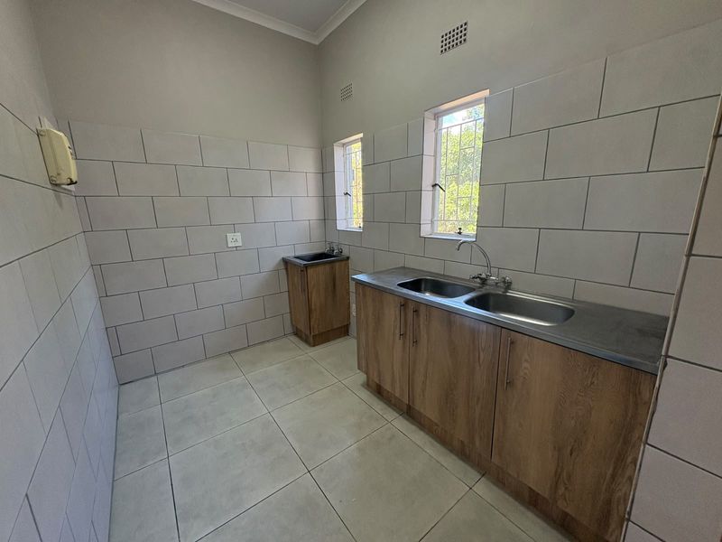 A clean and functional laundry room featuring tiled walls, ample built-in cabinetry, and double stainless steel sink basins.