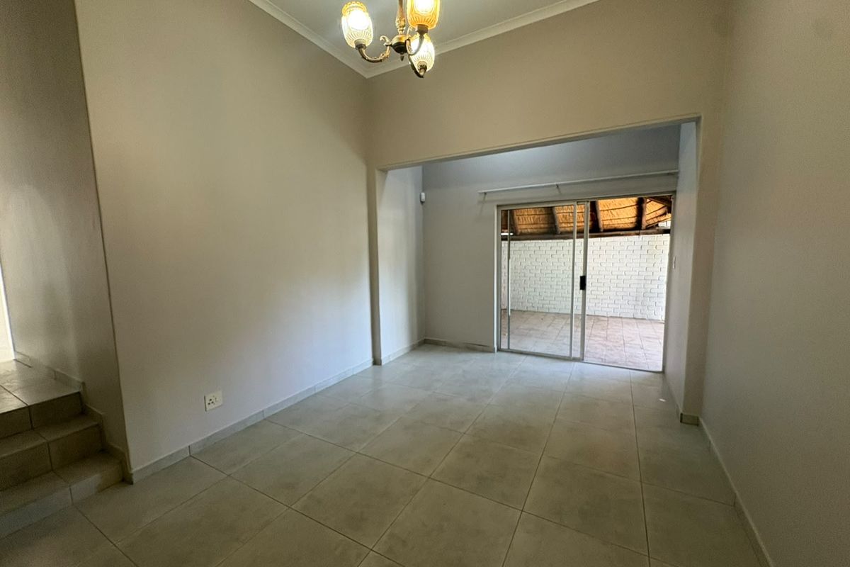An empty living area featuring neutral tiled flooring, a classic chandelier, and a sliding glass door providing access to an outdoor patio space.