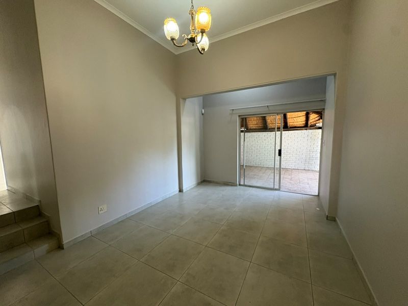 An empty living area featuring neutral tiled flooring, a classic chandelier, and a sliding glass door providing access to an outdoor patio space.