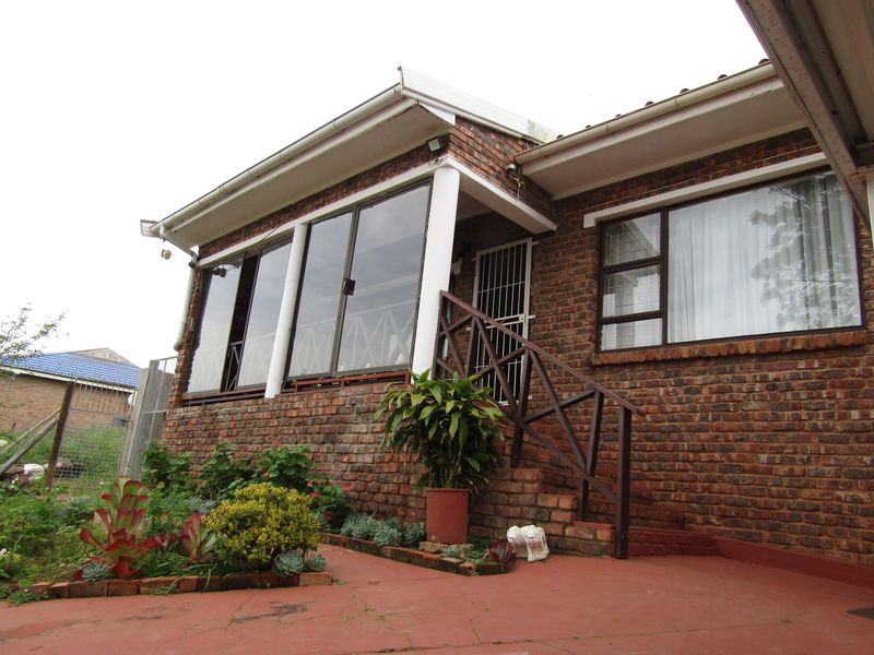 Rear view of a face brick house featuring a raised patio area, aluminium sliding doors, and a timber staircase leading to the entrance.