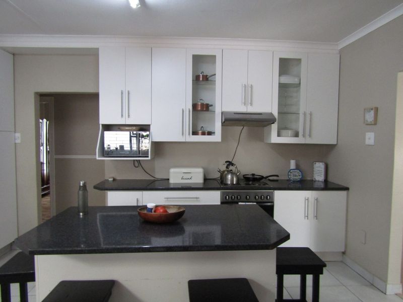 A functional kitchen featuring white cabinetry, dark granite countertops, a central island, and integrated appliances, offering a clean and practical workspace.