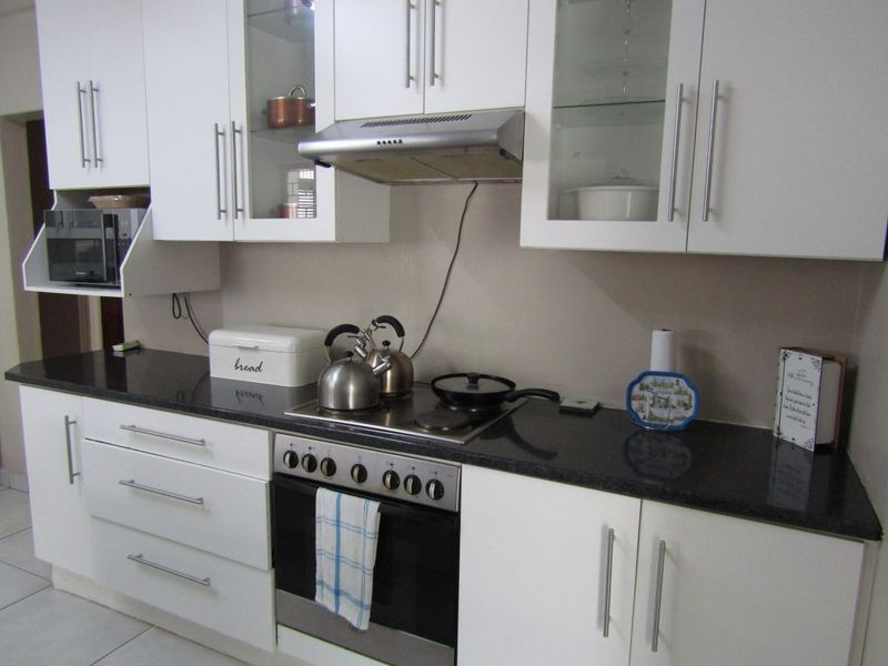 A functional kitchen featuring white cabinetry, dark granite countertops, and integrated stainless steel appliances including an oven, hob, and extractor fan.