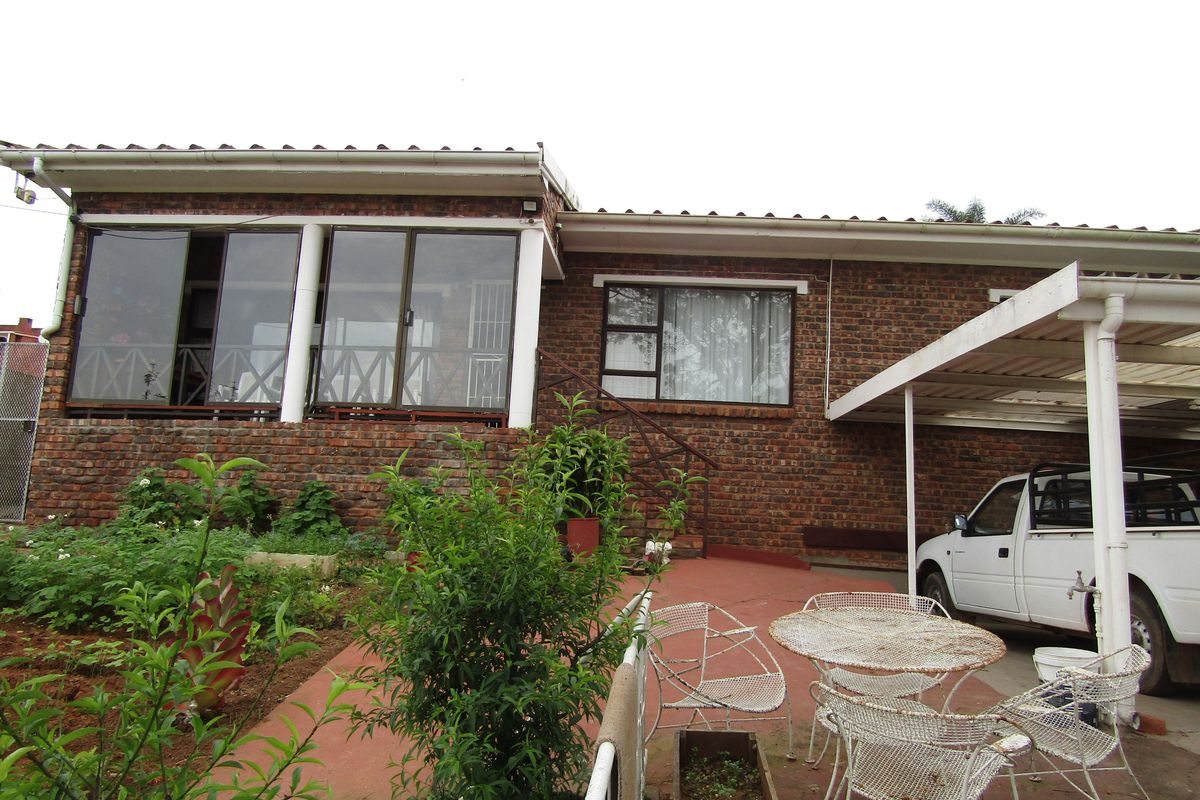 Rear view of a face brick house featuring a covered carport, concrete patio area, and aluminium sliding doors leading into the home.
