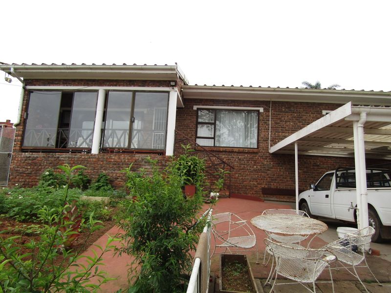 Rear view of a face brick house featuring a covered carport, concrete patio area, and aluminium sliding doors leading into the home.