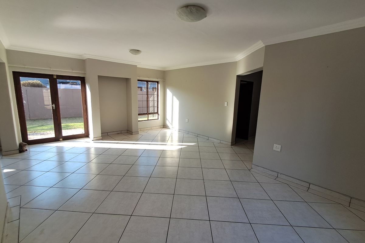 A spacious, empty living room featuring neutral tiled flooring, coved cornicing, and large french doors providing access to the garden area.