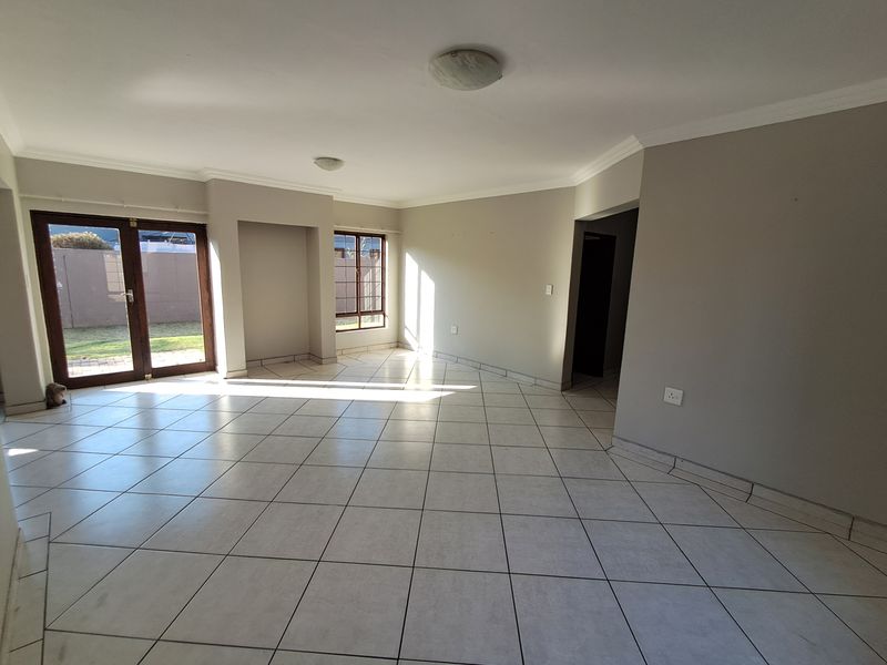 A spacious, empty living room featuring neutral tiled flooring, coved cornicing, and large french doors providing access to the garden area.