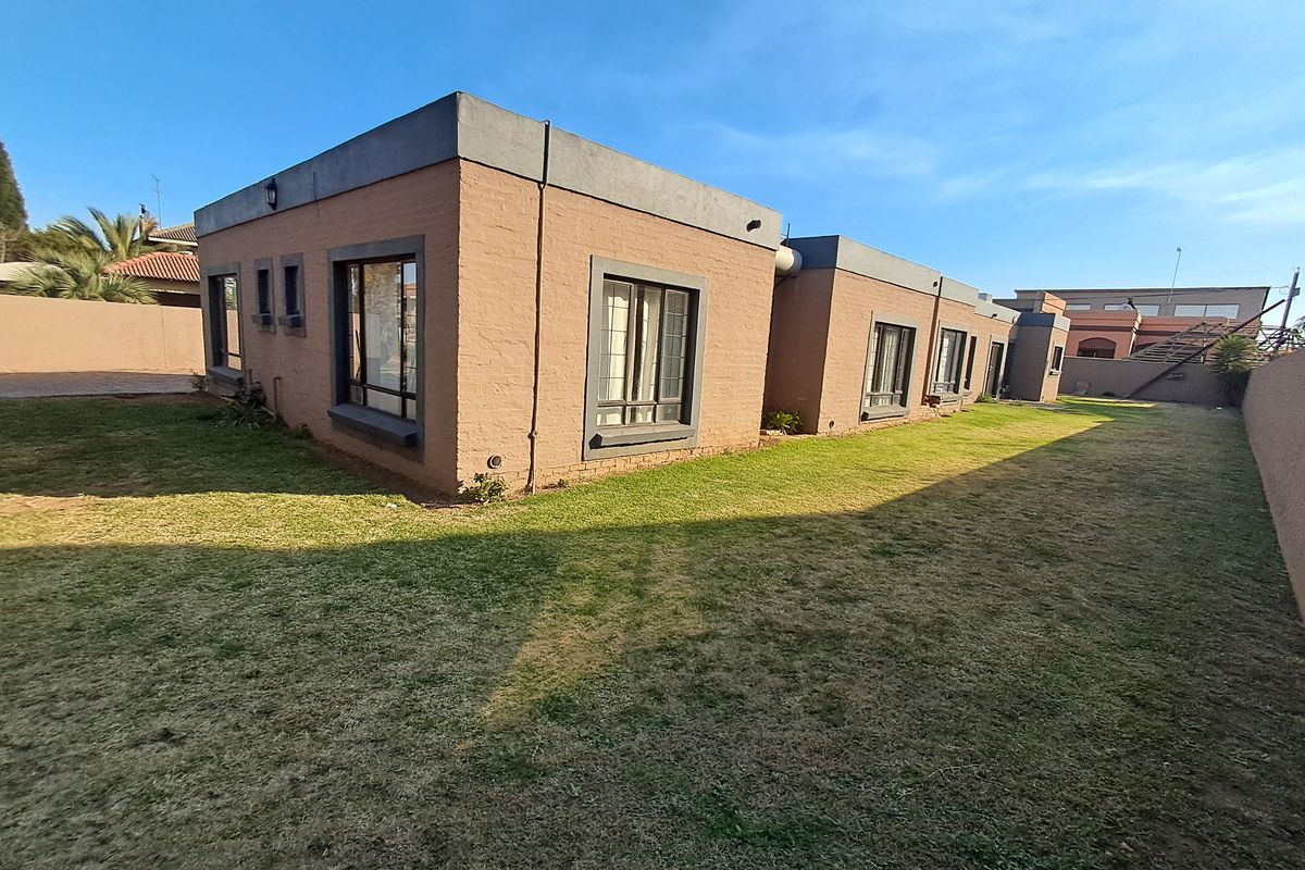 A view of the rear exterior of the house, featuring a brick facade, flat roof design, and a spacious surrounding lawn area.