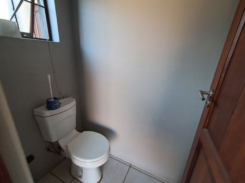 A compact bathroom featuring a standard toilet, tiled flooring, and a window, currently presenting in a dated condition.