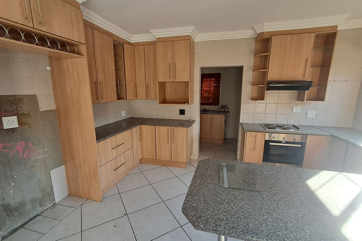 Spacious kitchen featuring light wood cabinetry, granite-look countertops, built-in oven and hob, and tiled flooring, requiring minor cosmetic finishing to the wall area.