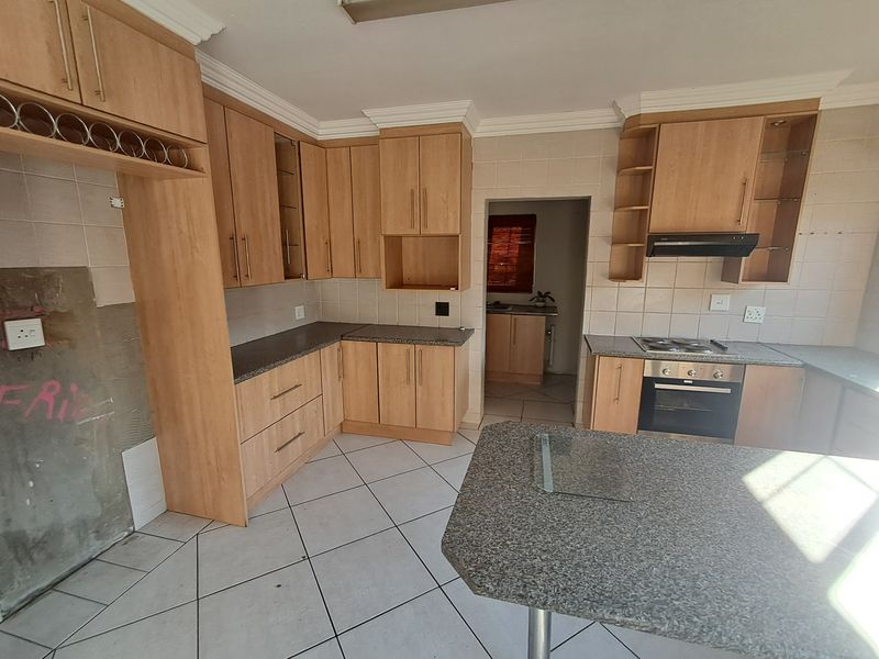 Spacious kitchen featuring light wood cabinetry, granite-look countertops, built-in oven and hob, and tiled flooring, requiring minor cosmetic finishing to the wall area.
