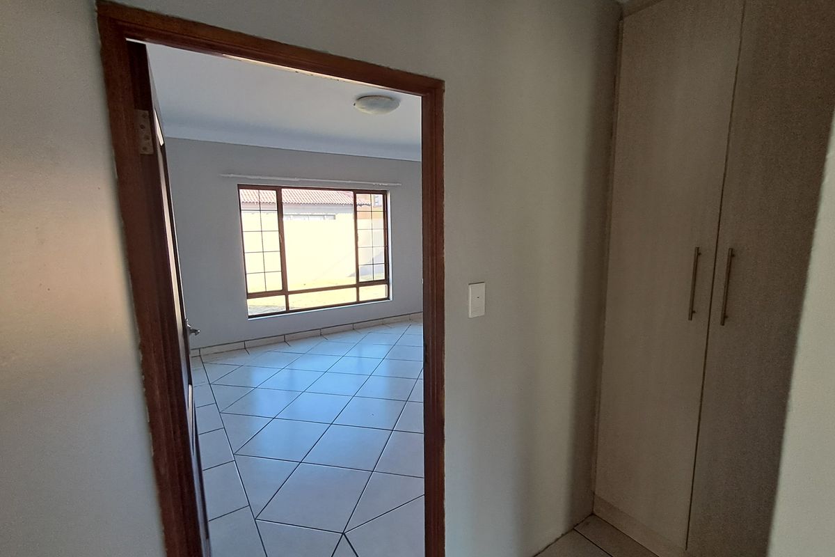 An empty bedroom featuring tiled flooring, built-in cupboards, and a window with security bars, offering a clean and neutral space.