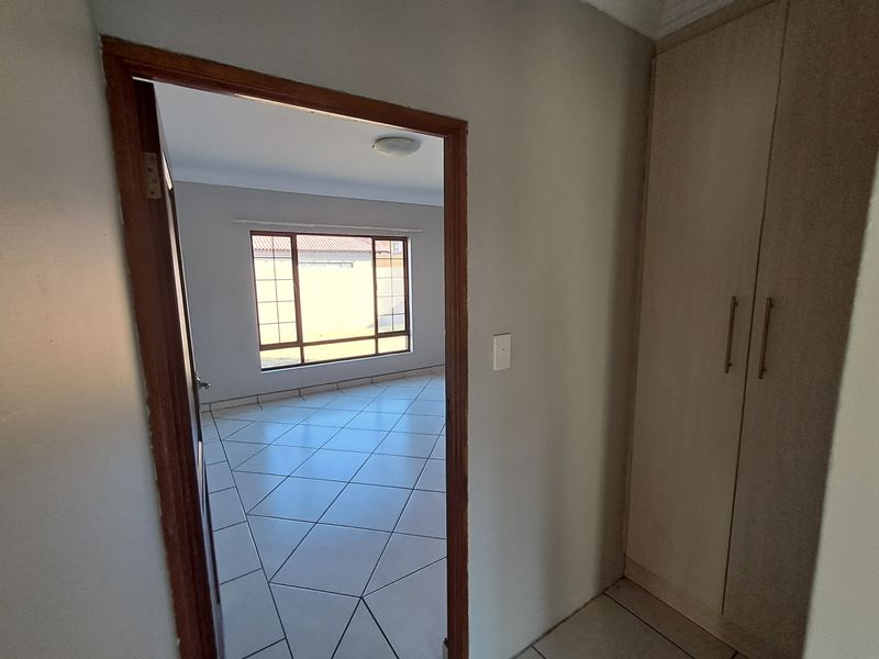 An empty bedroom featuring tiled flooring, built-in cupboards, and a window with security bars, offering a clean and neutral space.
