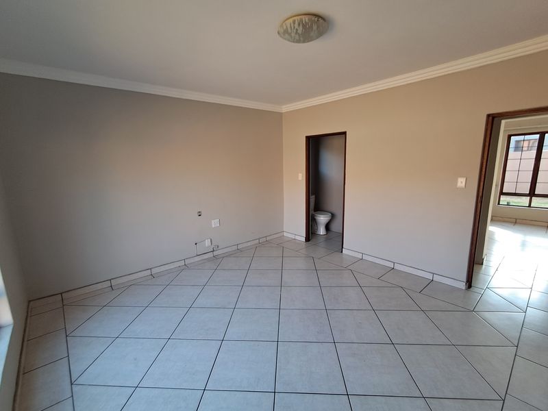 A spacious, empty bedroom featuring neutral tiled flooring, coved cornicing, and direct access to an en-suite bathroom.