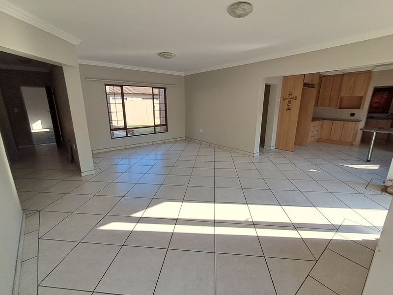 Spacious open-plan living and kitchen area featuring neutral tiled flooring, ample natural light, and functional built-in cabinetry.