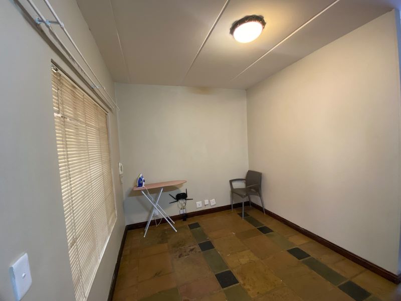 A simple, empty bedroom featuring tiled flooring, venetian blinds, and a ceiling light fixture, offering a blank canvas for potential renovation or staging.