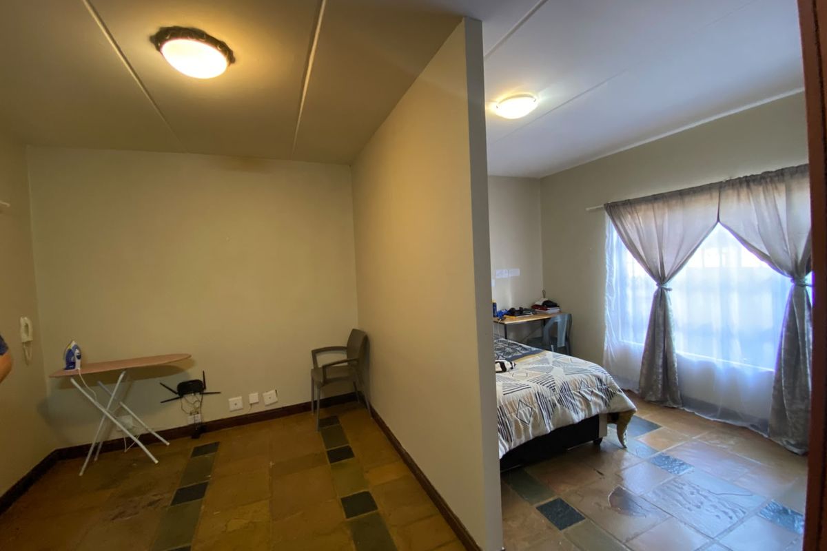A bedroom area featuring a partition wall, tiled flooring, and natural light through a window with curtains.