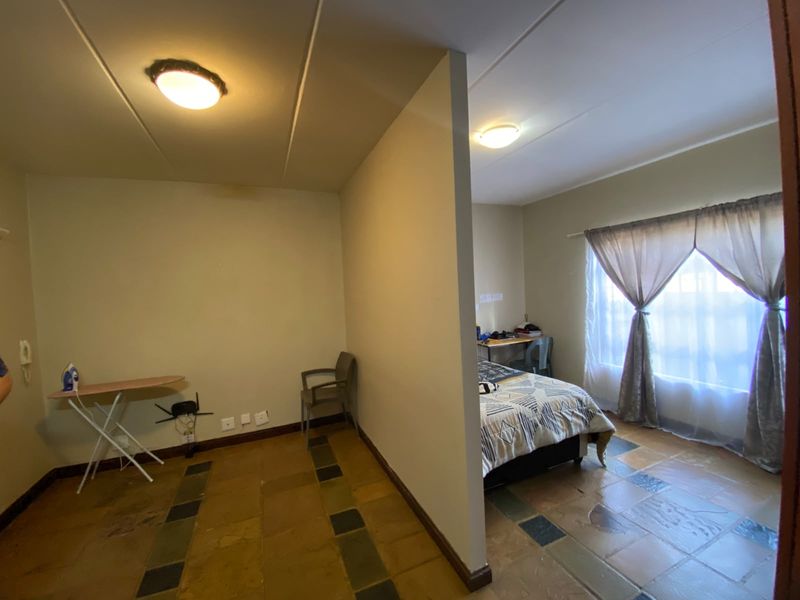 A bedroom area featuring a partition wall, tiled flooring, and natural light through a window with curtains.