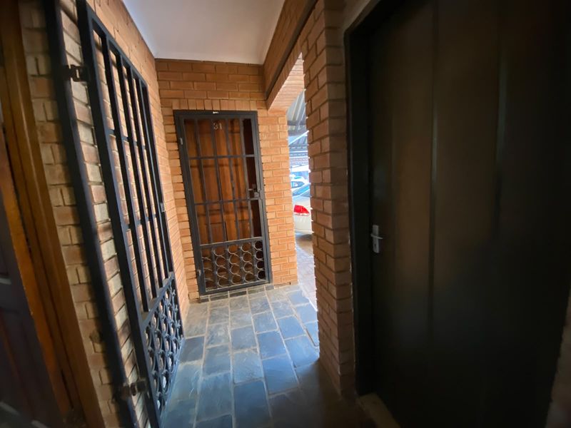 Entrance area featuring exposed brick walls, slate tile flooring, and a secure metal gate leading to the main apartment door.