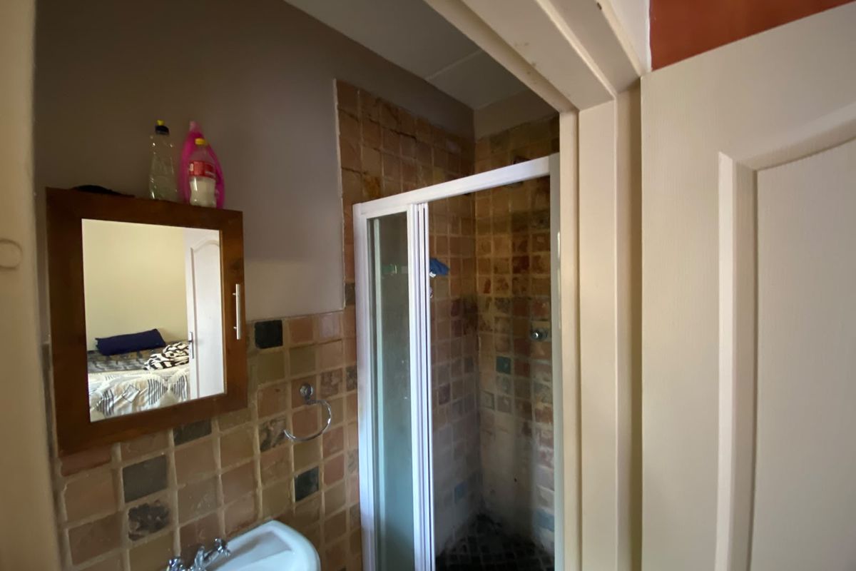 A compact bathroom featuring a shower enclosure, pedestal basin, and wall-mounted mirror with dated tiled finishes throughout.