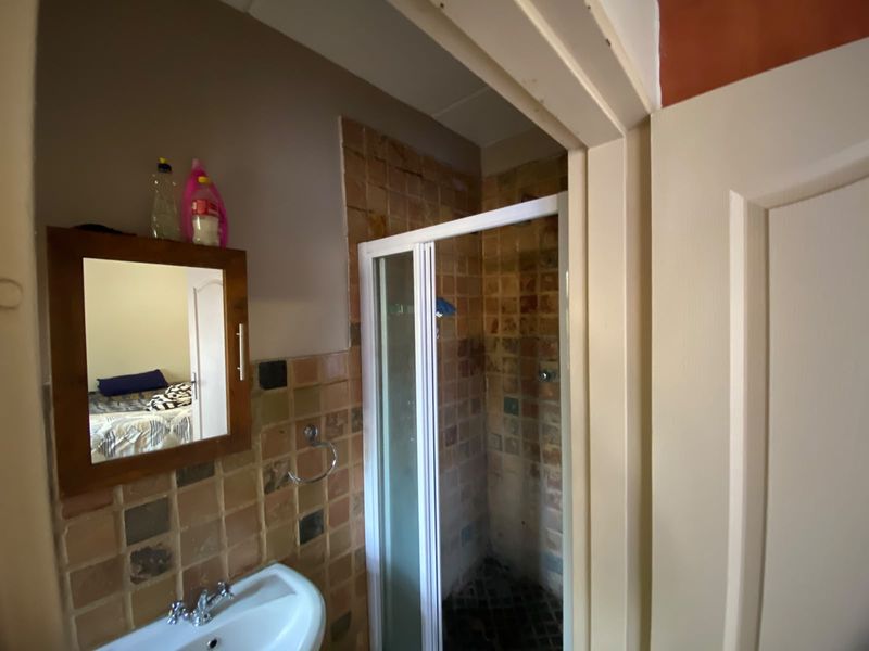 A compact bathroom featuring a shower enclosure, pedestal basin, and wall-mounted mirror with dated tiled finishes throughout.