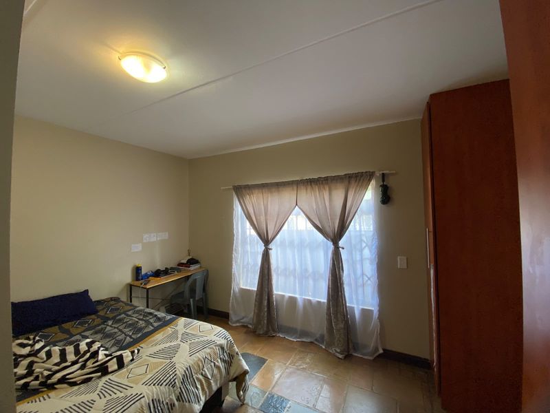 A functional bedroom featuring tiled flooring, a built-in wardrobe, and a window fitted with a security gate, providing natural light and essential storage.
