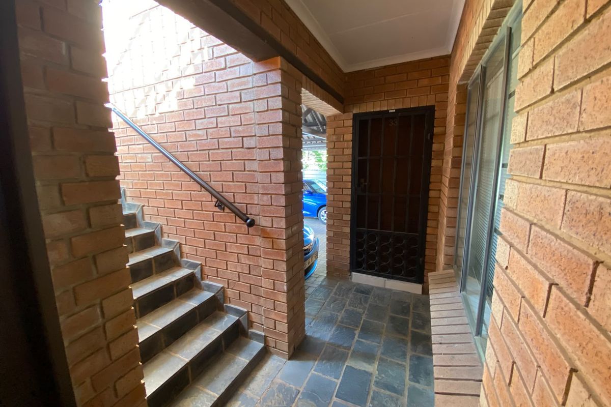 A private entrance area featuring exposed brick walls, stone tile flooring, and a secure metal gate leading to the apartment.