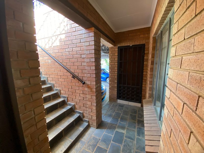 A private entrance area featuring exposed brick walls, stone tile flooring, and a secure metal gate leading to the apartment.