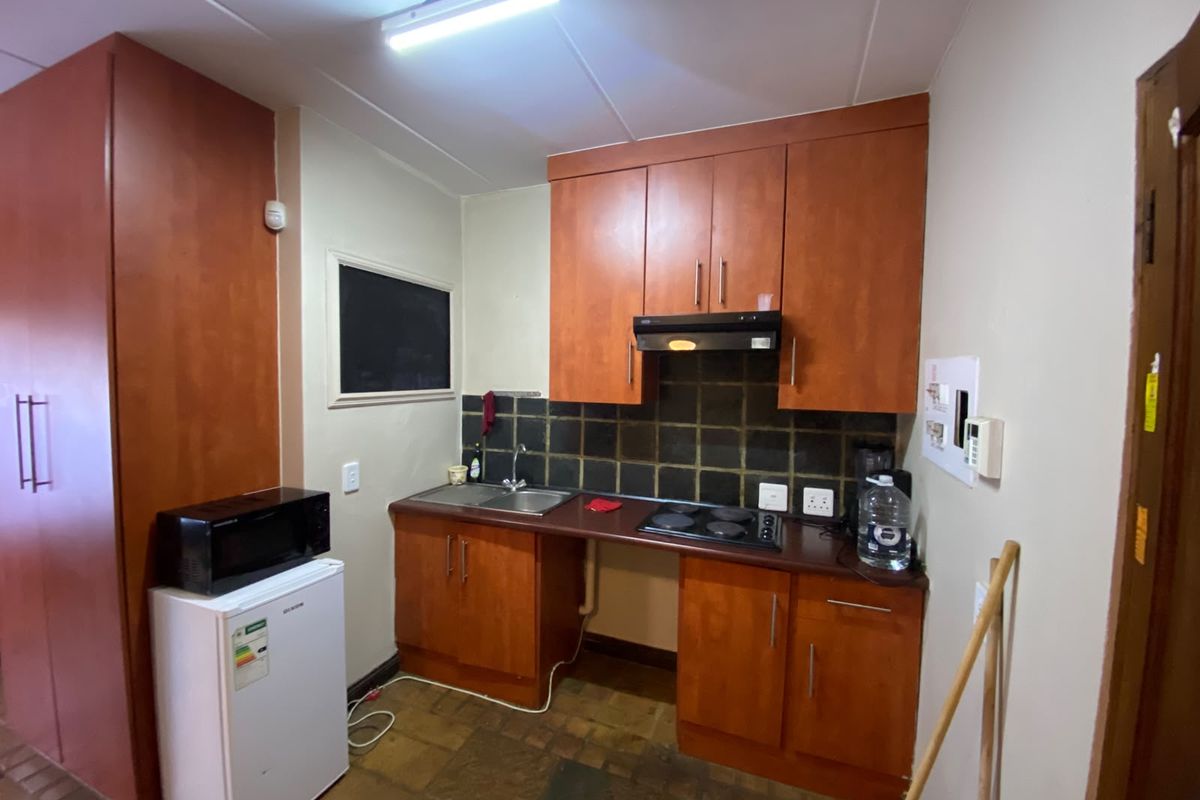 Compact kitchen featuring wood-finish cabinetry, built-in electric hob with extractor fan, tiled backsplash, and stainless steel sink.