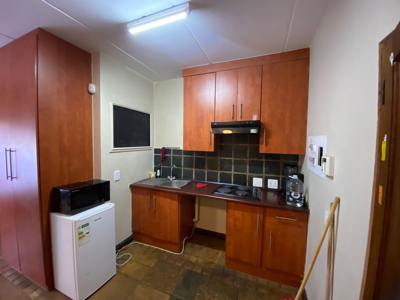 Compact kitchen featuring wood-finish cabinetry, built-in electric hob with extractor fan, tiled backsplash, and stainless steel sink.