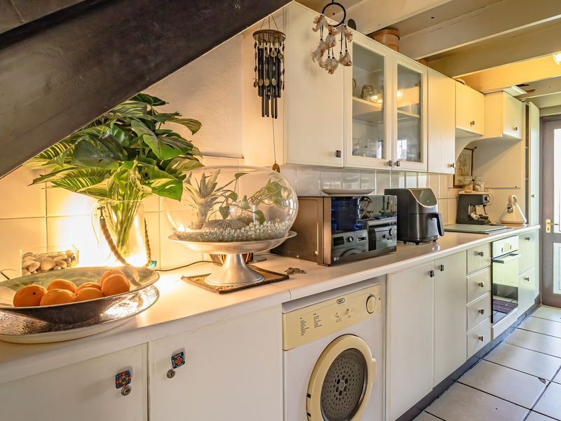 A functional kitchen featuring white cabinetry, tiled flooring, and integrated appliances, with direct access to the exterior via a glass-paneled door.