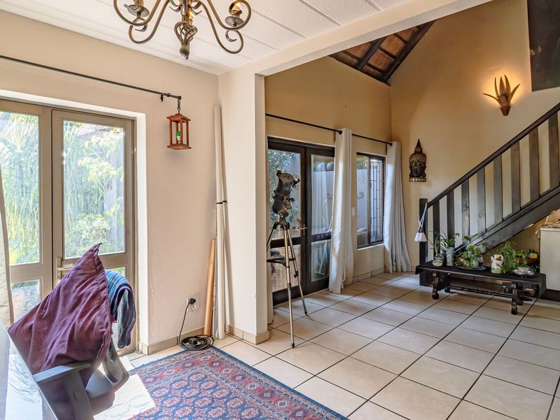 Spacious living area featuring tiled flooring, a vaulted ceiling with exposed timber beams, and a staircase with a wooden balustrade leading to the upper level.