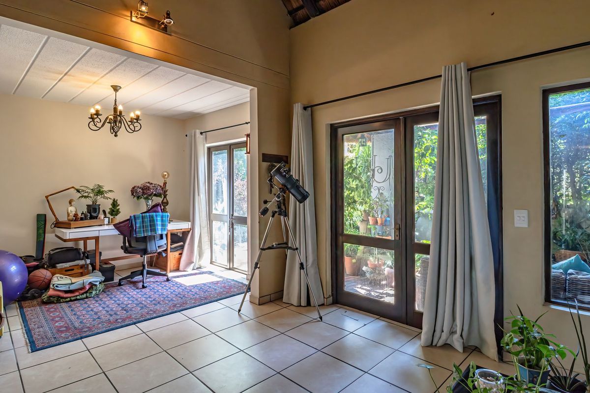 Spacious living area featuring tiled flooring, vaulted ceilings with exposed beams, and large glass doors providing ample natural light and garden access.