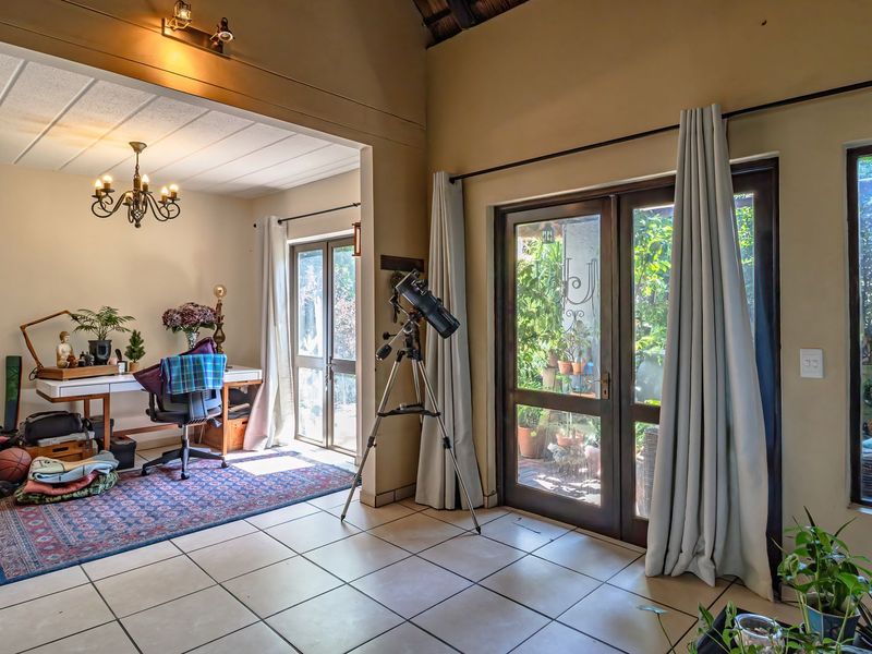 Spacious living area featuring tiled flooring, vaulted ceilings with exposed beams, and large glass doors providing ample natural light and garden access.