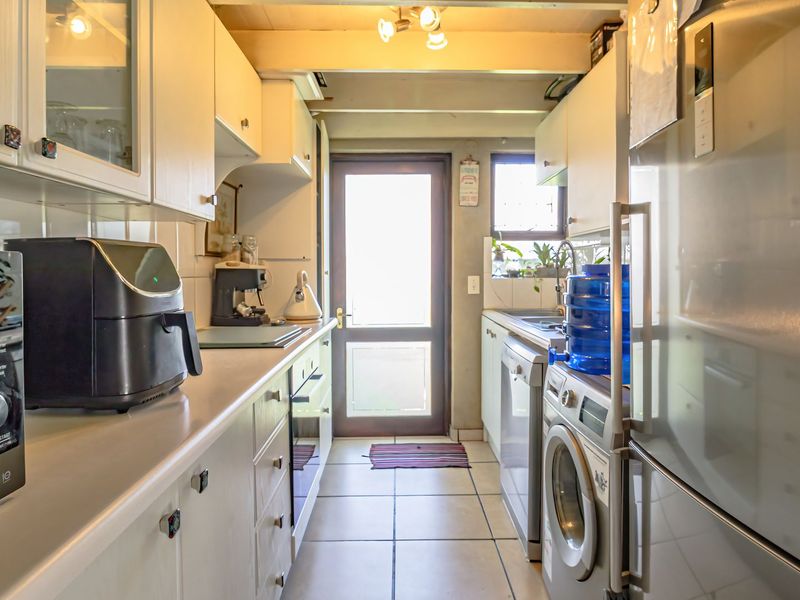 A functional galley-style kitchen featuring white cabinetry, tiled flooring, and direct access to the exterior, offering a practical layout for daily meal preparation.