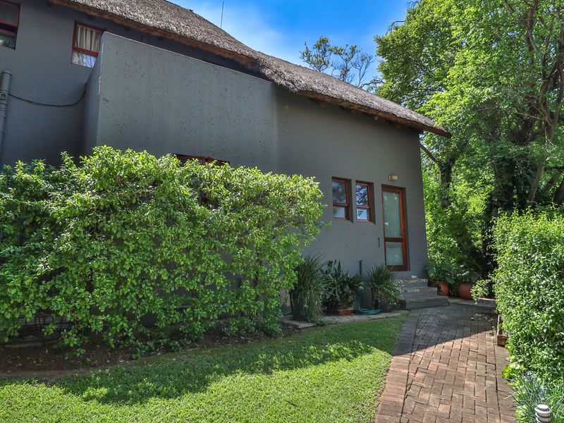Rear view of the townhouse featuring a traditional thatch roof, paved garden walkway, and mature landscaping surrounding the exterior facade.