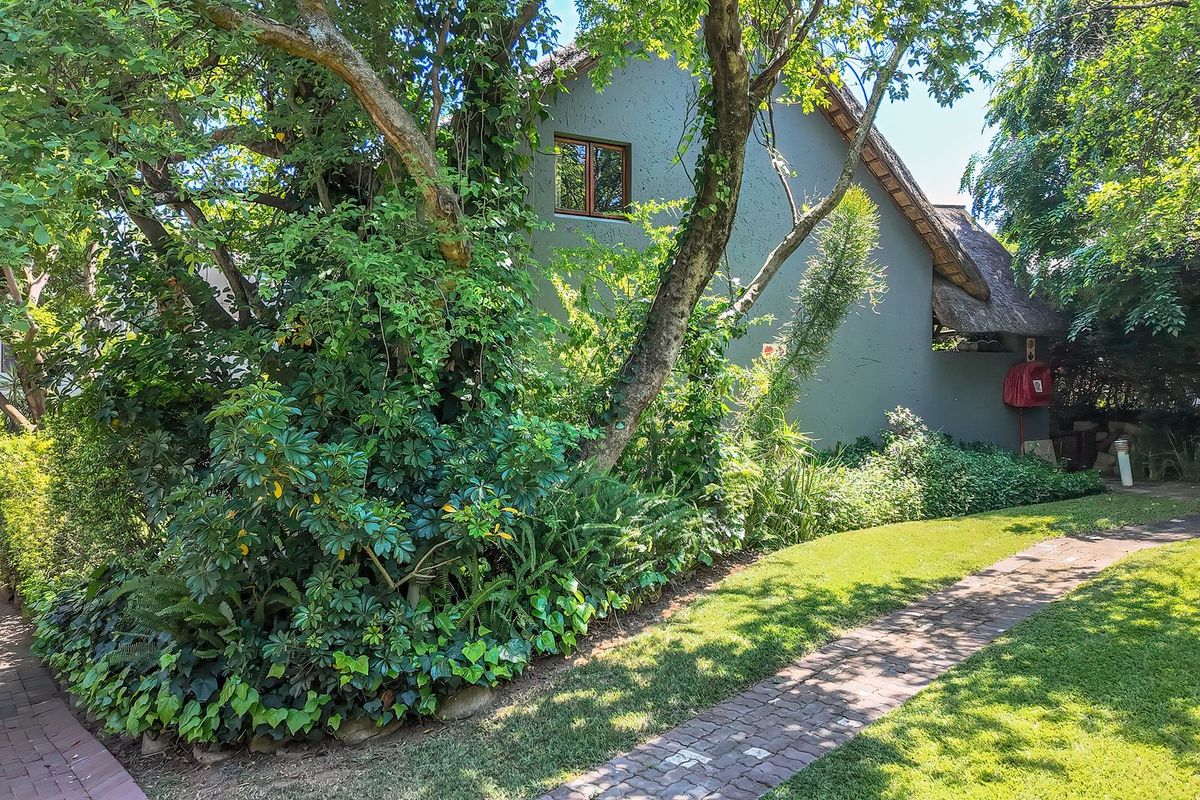 A view of the rear exterior of the townhouse featuring a thatched roof, brick paved pathway, and established garden landscaping.