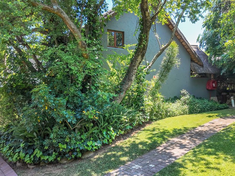 A view of the rear exterior of the townhouse featuring a thatched roof, brick paved pathway, and established garden landscaping.